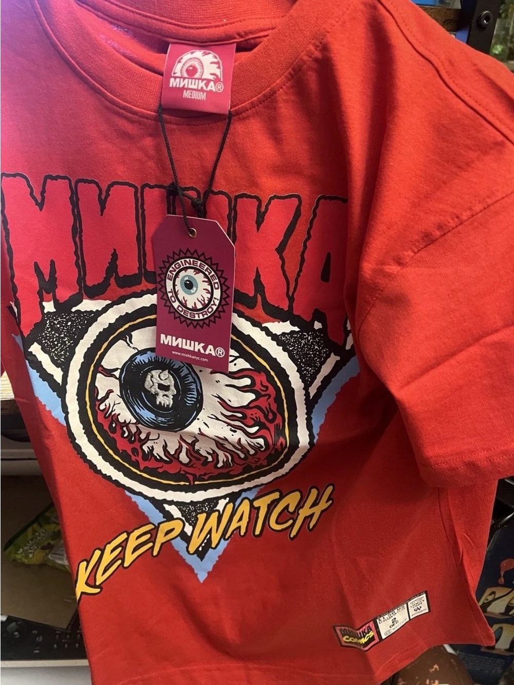 Mishka red tee with the Keep Watch eye graphic and an embroidered skull, size M